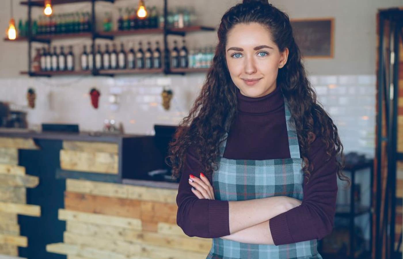A small business owner standing with arms crossed behind the counter of her coffee shop