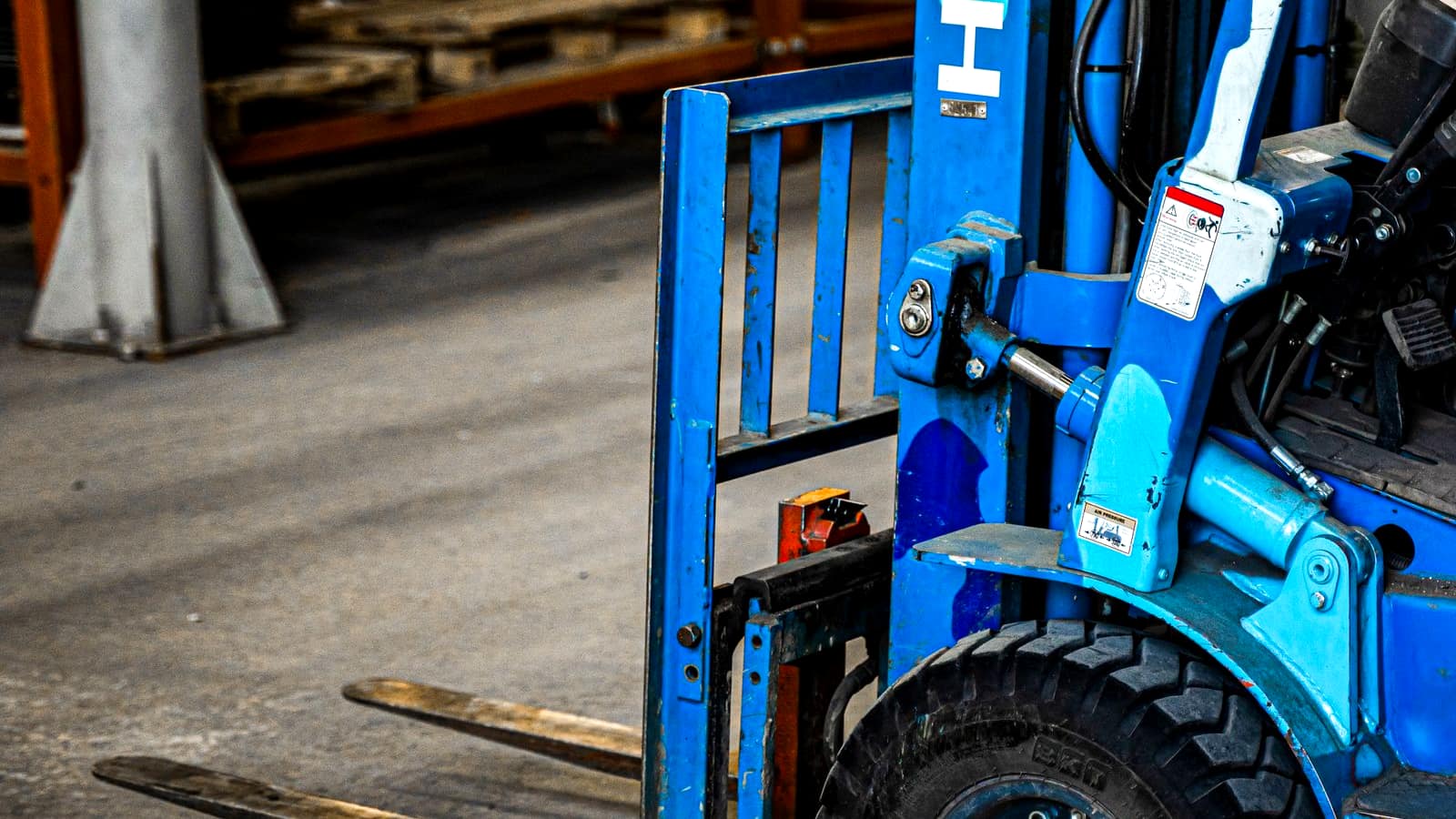 A close-up of a blue forklift's mast and forks on a warehouse floor