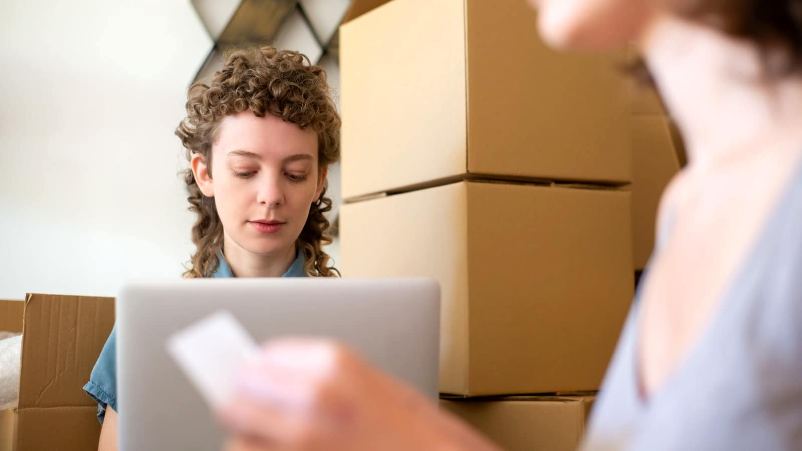 A small business owner with a laptop working among stacked shipping boxes