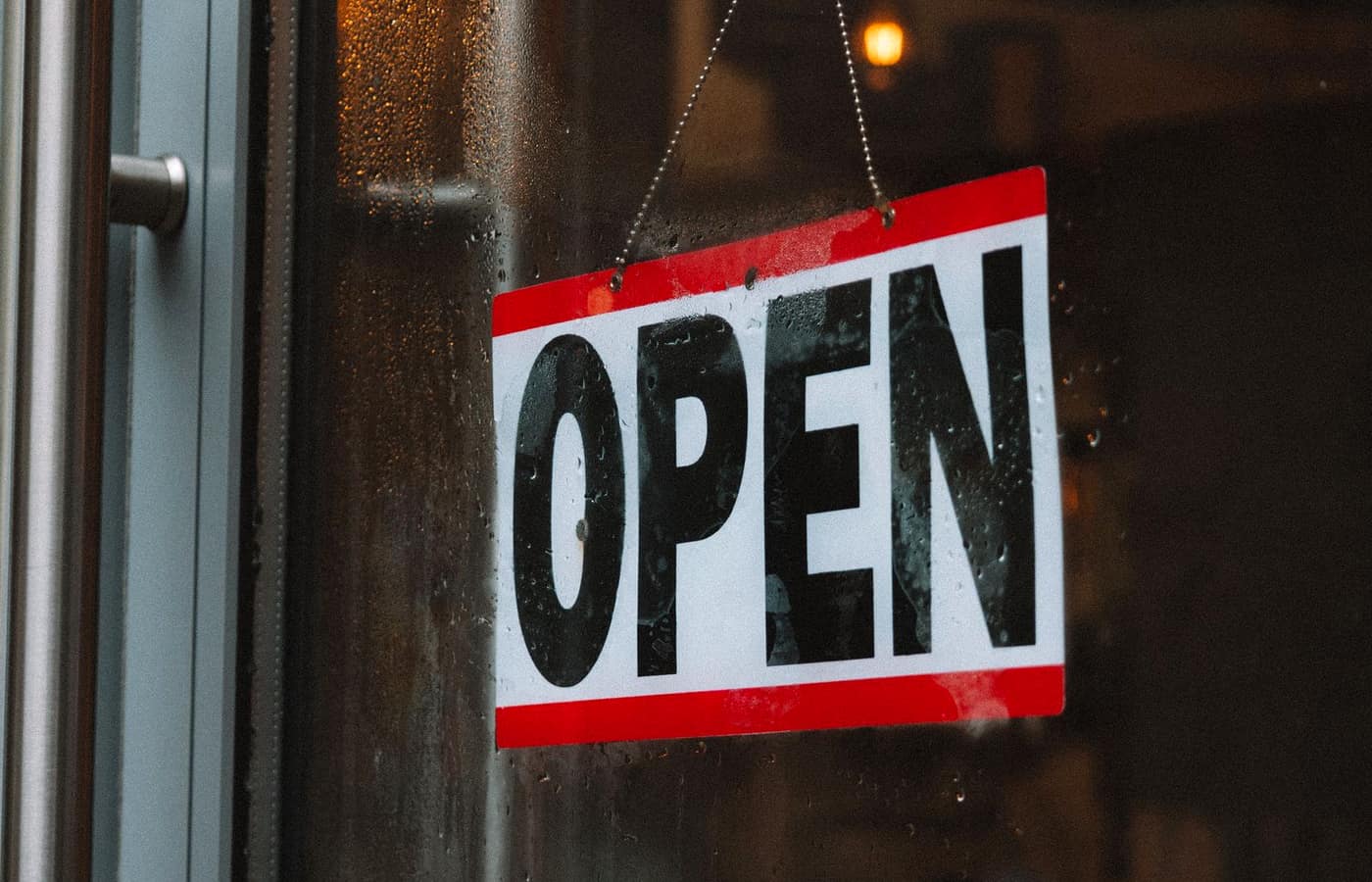 A red and white OPEN sign hanging on the glass door of a shop.