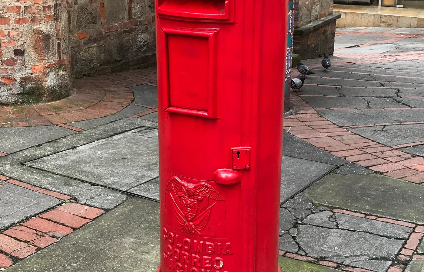 A red pillar-box mailbox on a cobbled street.