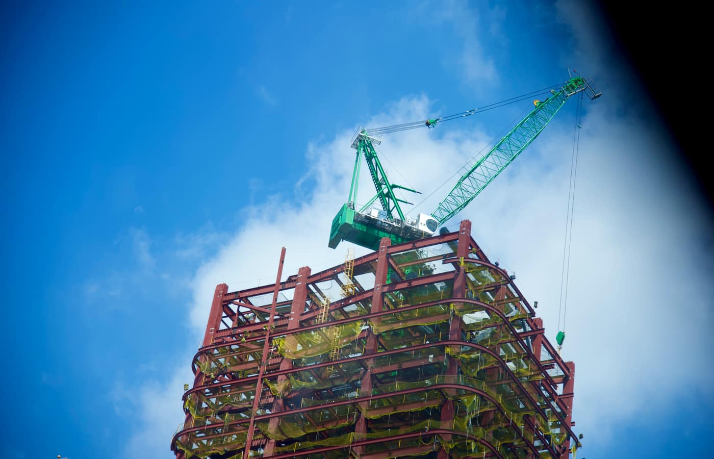 A steel-frame commercial building under construction with a tower crane against a blue sky.