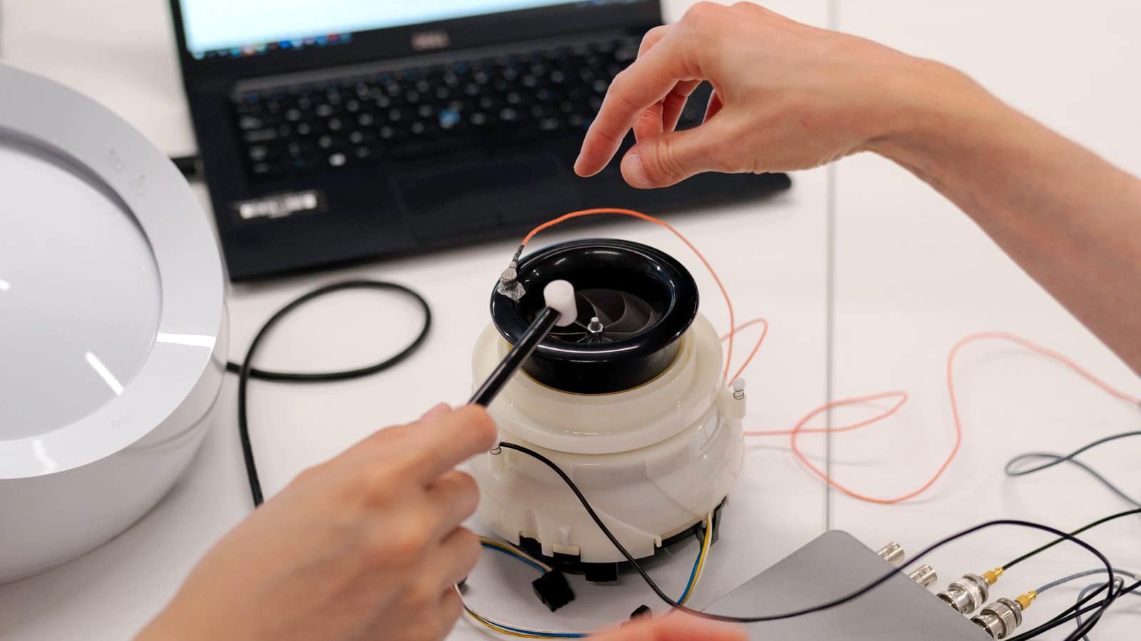 Two people working on an electronic prototype device with wires and a laptop on a workbench