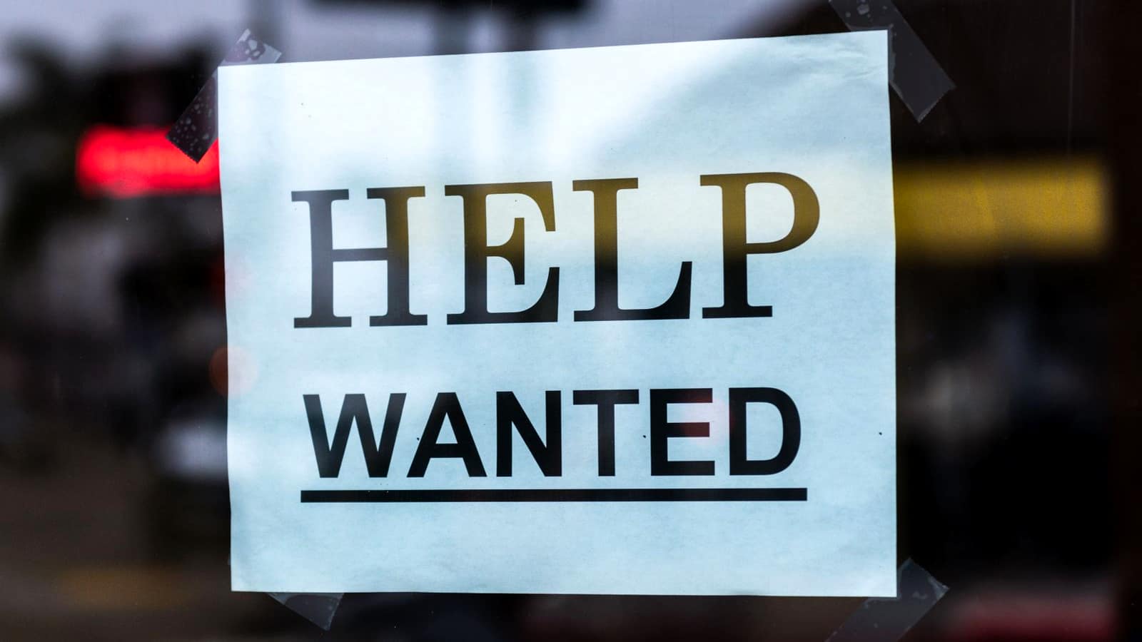 A hand-lettered Help Wanted sign taped inside a storefront window