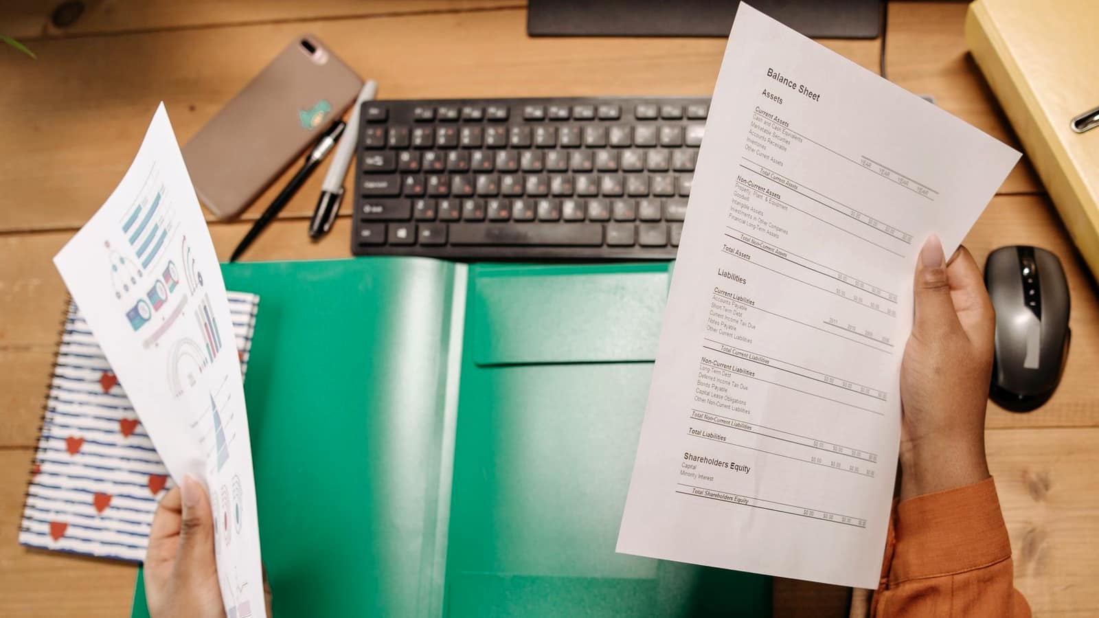 A person reviewing a printed financial statement over a desk with a keyboard and notes